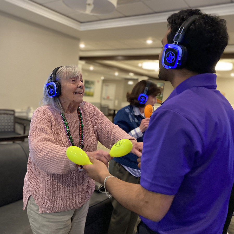 A memory care resident dances with a volunteer, lost in the rhythm. With headphones on, they enjoy music together.