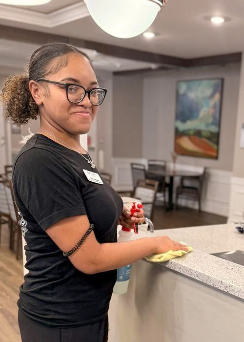 Team member smiling while wiping down a counter during spring cleaning at a senior living community.