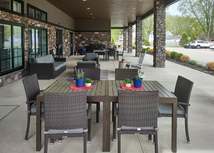 Outdoor covered patio at a senior living community with modern dining tables, potted plants, and cozy seating areas for resident gatherings.
