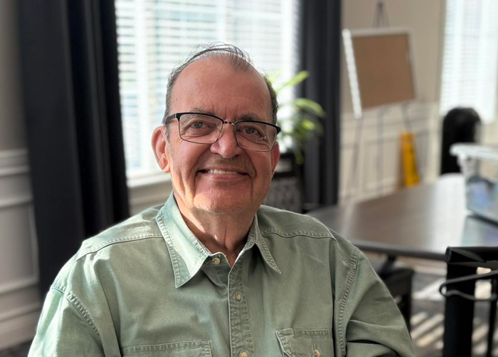 Man in green shirt smiling while seated near a window in a senior living community common room