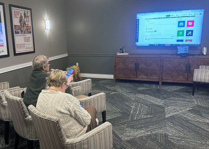 Two senior residents viewing a large screen and engaging with a tablet during a technology workshop.