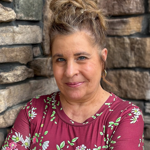 Gretchen Banak, Business Office Director at Vitalia North Olmsted, wearing a burgundy floral blouse, smiling in front of a stone wall.