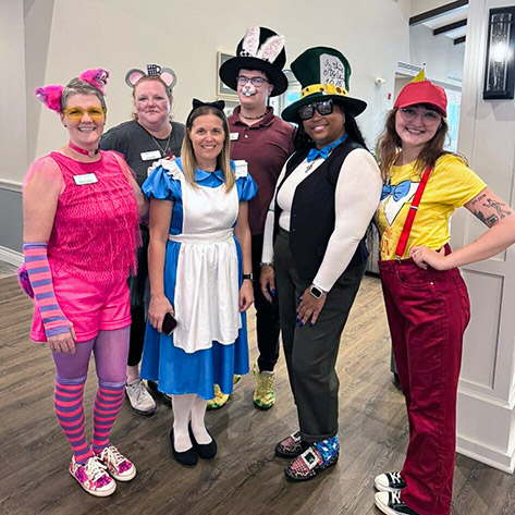 A group of team members in highly themed costumes smile during a celebration for a resident centenarian.