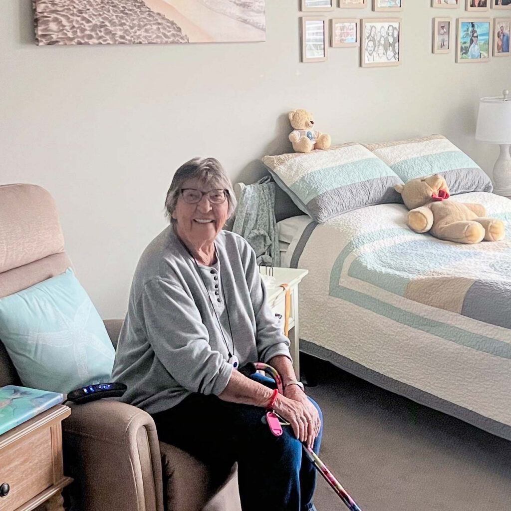A senior woman smiles in her apartment, showcasing personal touches in many pastels.