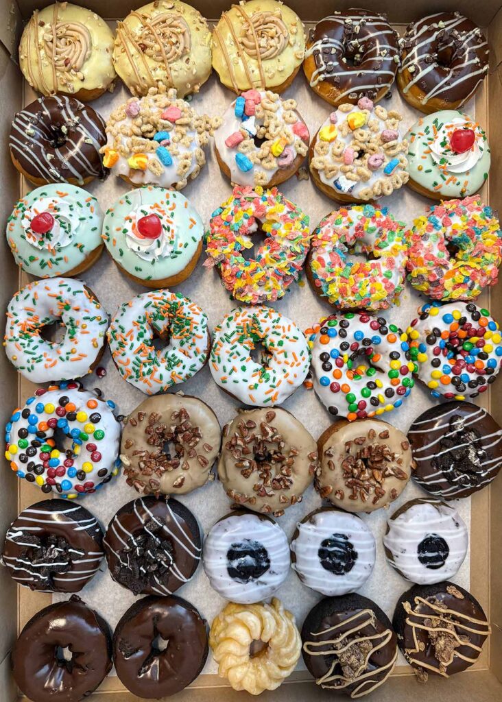 A vast selection of assorted gourmet doughnuts from a local business.